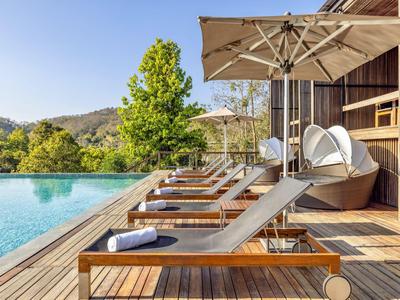 Moderne Pool-Liegeplätze mit Holzboden und Sonnenschirmen vor einer Holzhütte mitten in der Natur.