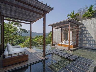 Moderner Außenbereich mit Pool, Liegestühlen und überdachten Sitzbereichen mit Blick auf bewaldete Hügel.