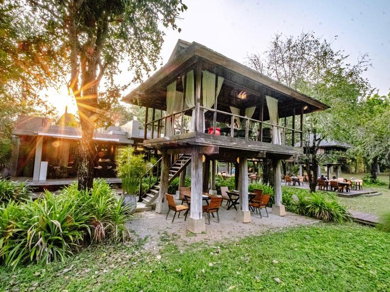 Modernes Baumhaus-Hotel mit großer Veranda in grüner Natur bei Sonnenuntergang