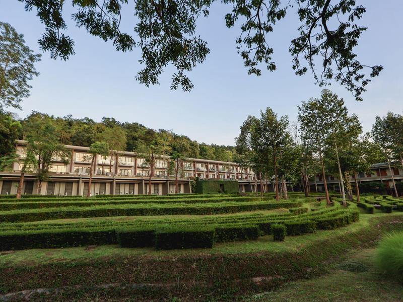 Großes Hotelgebäude mit gepflegtem Garten und dekorativem Heckenmuster bei klarem Himmel.