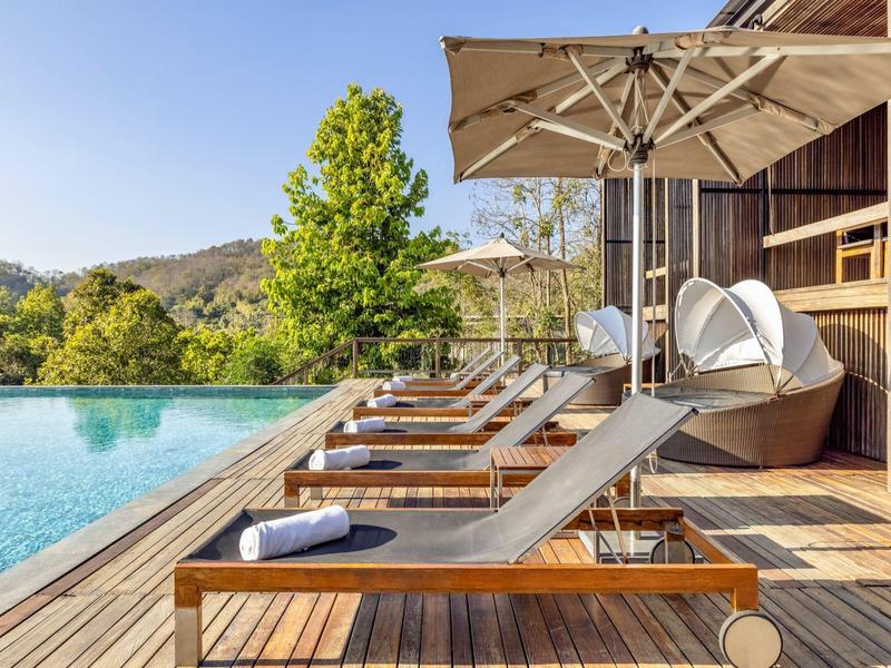 Holzdeck mit Liegestühlen und Sonnenschirmen neben einem Pool in sonniger Landschaft