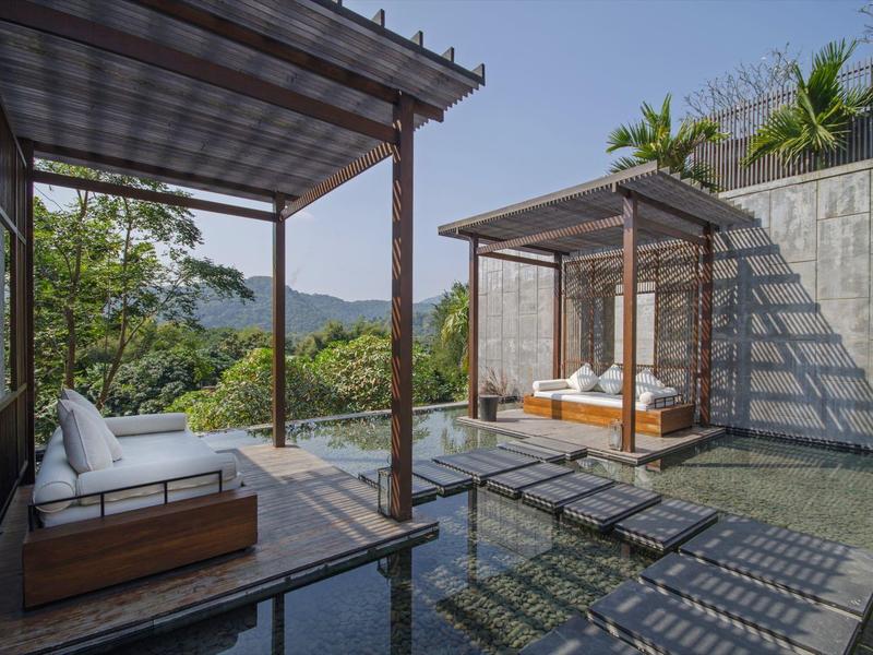 Moderner Außenbereich mit Pool, Liegestühlen und überdachten Sitzbereichen mit Blick auf bewaldete Hügel.