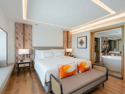 Modernes Hotelzimmer mit großem Bett, Sitzbank, Holzfußboden und offenem Badezimmer.