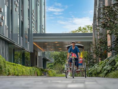 Zwei Menschen fahren mit einem Fahrrad zwischen modernen Gebäuden auf einem gepflasterten Weg.
