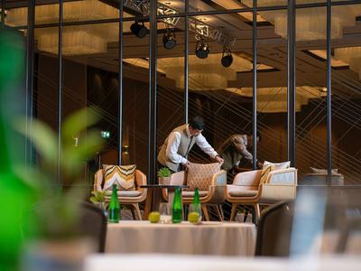 Mann deckt Tisch mit weißen Stühlen in modernem, gemütlichem Restaurant mit warmem Licht.