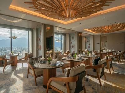 Elegantes Restaurant mit großen Fenstern, Holzstühlen und dekorativer Decke mit Blick auf die Berge.