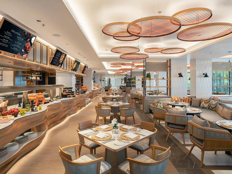 Modernes Restaurant mit elegantem Holzmobiliar, runden Tischen und großen Fenstern für viel Licht.