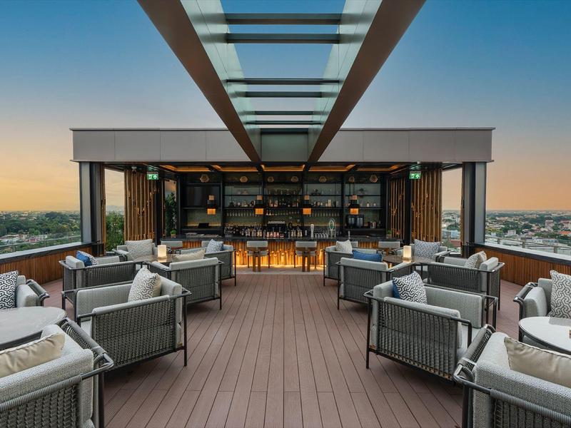 Dachterrasse mit Sitzgruppen und modernem Glasdach bei Sonnenuntergang, weiter Stadtblick.