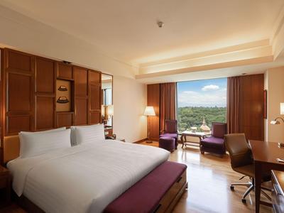 Helles Hotelzimmer mit großem Bett, Schreibtisch, Sesseln und Blick auf grüne Landschaft.