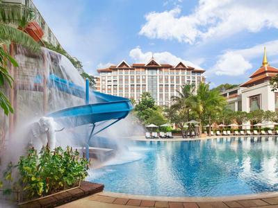 Velký hotelový bazén s tobogánem a vodopádem před vícepodlažní hotelovou budovou pod slunečnou oblohou