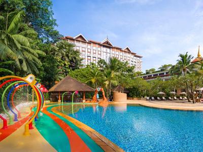 Großer Pool mit Wasserfontänen und tropischer Vegetation in einem Hotelresort.