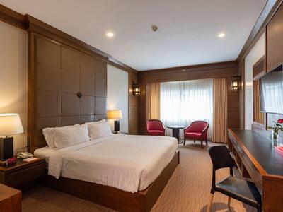 Gemütliches Hotelzimmer mit großem Bett, Schreibtisch und zwei roten Sesseln am Fenster.