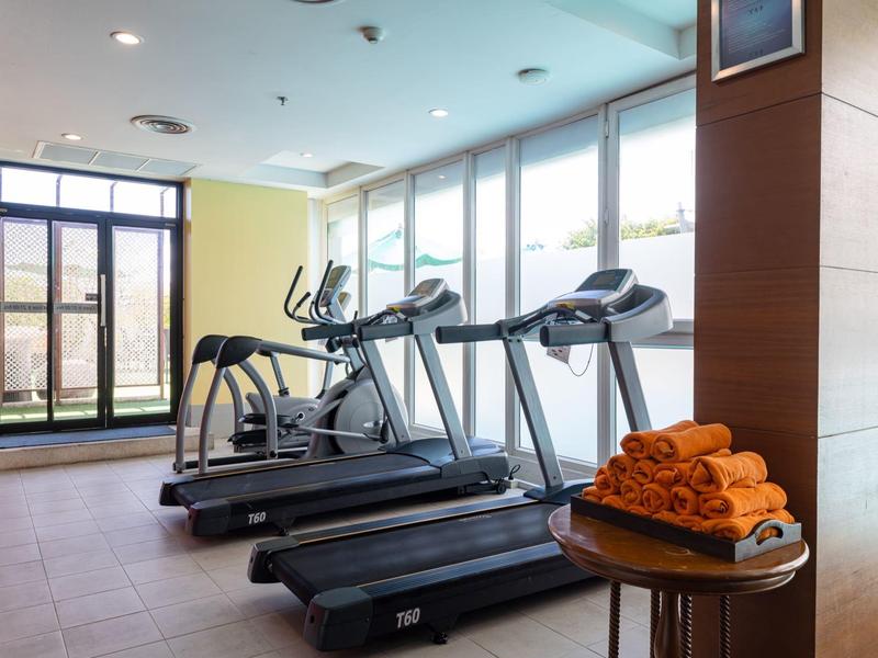 Fitnessraum mit Laufbändern und einem Ellipsentrainer vor großen Fenstern mit Tageslicht.