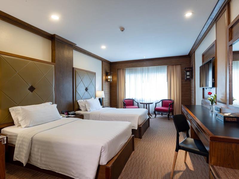 Hotelzimmer mit zwei Einzelbetten, Holzvertäfelung, Schreibtisch und großem Fenster mit Vorhängen.