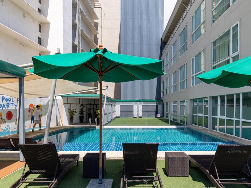 Moderner Hotelpool zwischen Gebäuden mit Liegestühlen und grünen Sonnenschirmen.