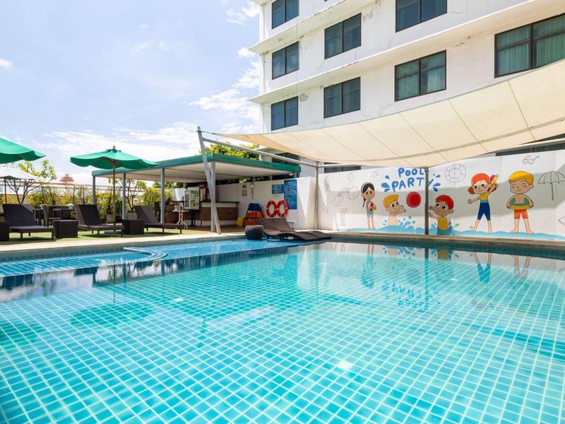 Klares Schwimmbecken mit Sonnenschirmen und einer Wand mit farbenfrohen Zeichnungen neben einem Hotelgebäude.
