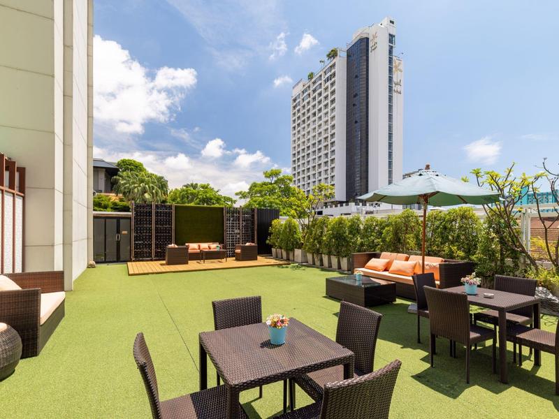 Dachterrasse mit Sitzplätzen, Sonnenschirmen und Aussicht auf ein Hochhaus bei klarem Himmel.