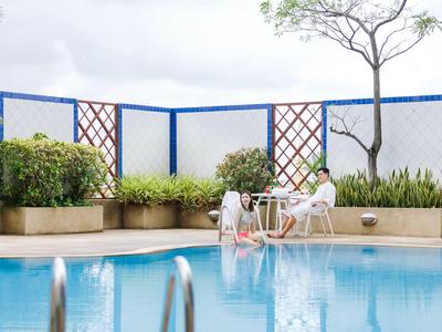 Person entspannt am Pool mit Getränken auf Tisch neben blauen Wänden und grünen Pflanzen.