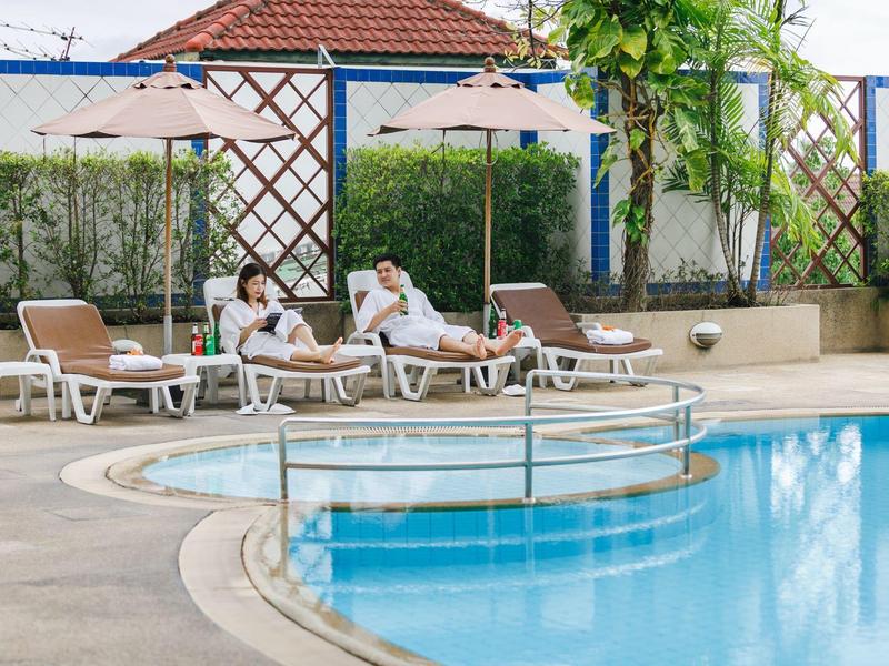 Zwei Personen entspannen auf Liegestühlen neben einem klaren Pool mit Sonnenschirmen.