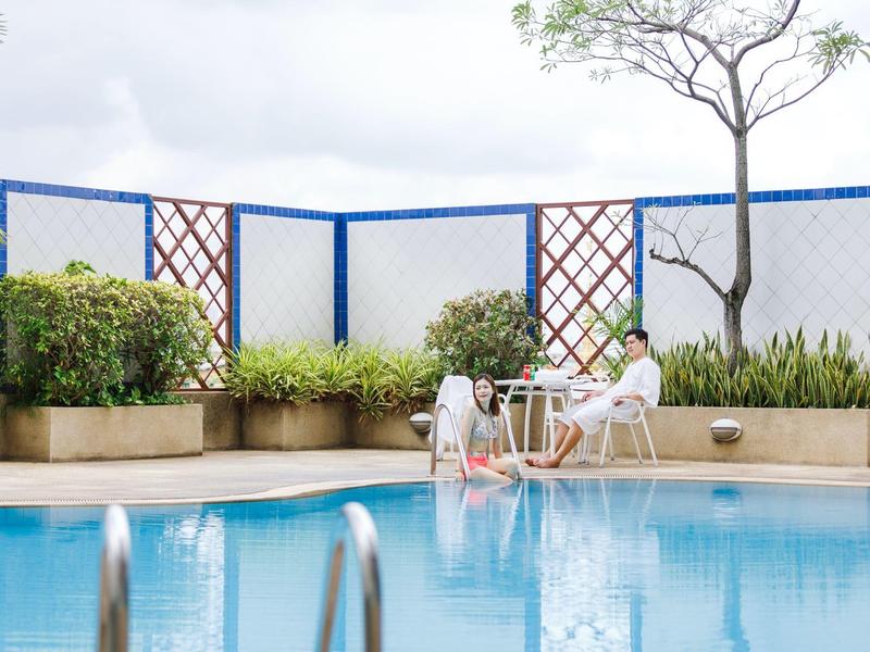 Zwei Frauen sitzen an einem Tisch neben einem Pool auf einer Terrasse mit Pflanzen und Gittern.