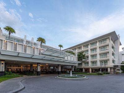 Modernes Hotel mit kreisrundem Eingangsbereich und Palmen auf dem Dach bei bewölktem Himmel.