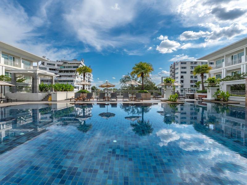 Moderner Poolbereich mit klaren blauen Wasser und umliegenden Hotelgebäuden unter wolkigem Himmel.