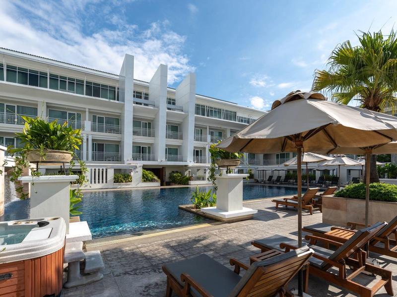 Hotel mit Pool, Sonnenschirmen und Liegestühlen unter blauem Himmel.