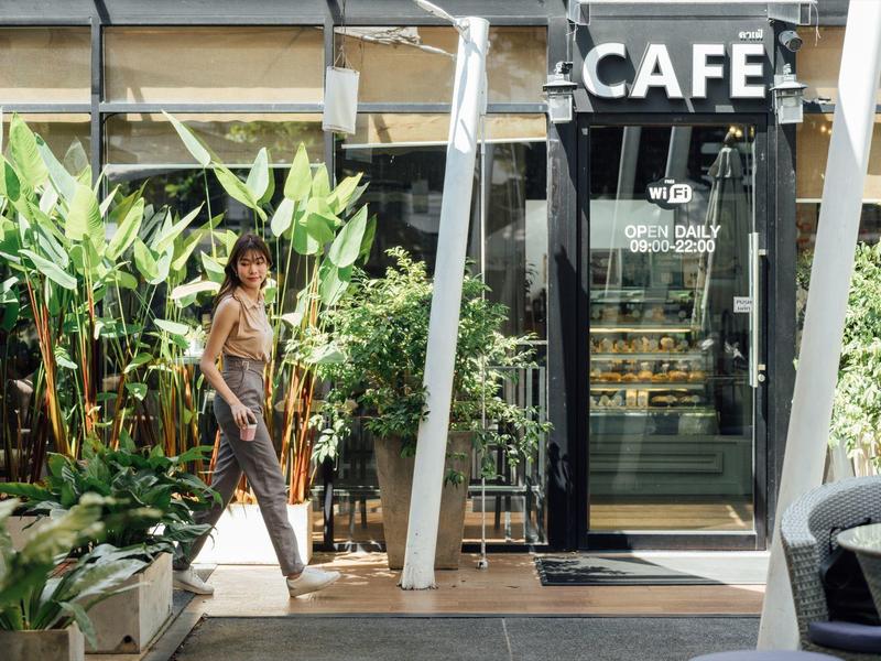 Frau geht an einem belebten Café mit vielen grünen Pflanzen vorbei.