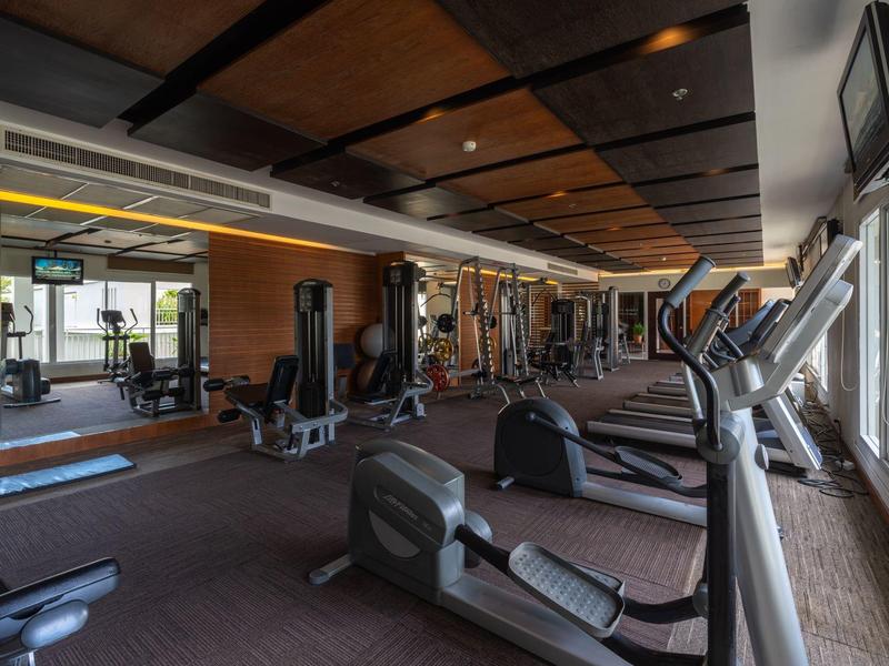 Modernes Fitnessstudio mit Geräten und großen Fenstern, die Tageslicht hereinlassen.