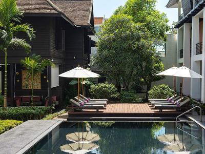 Moderní hotelový bazén s lehátky a slunečníky mezi budovami a stromy.