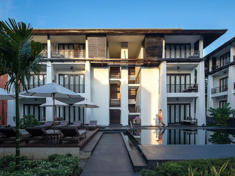 Modernes Hotel mit Pool, Sonnenliegen und Palmen bei klarem Himmel.