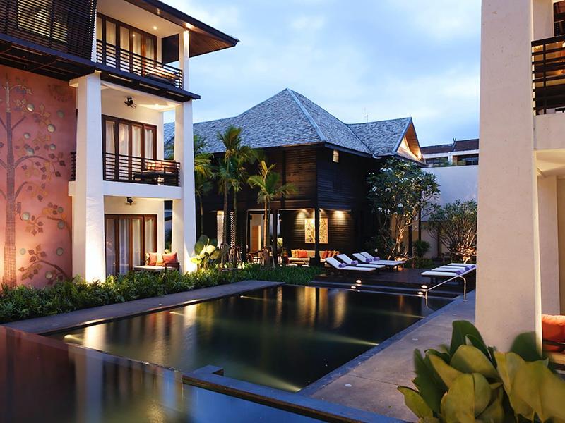 Lichtdurchflutetes Hotel mit Pool und Liegen, umgeben von modernen Gebäuden und tropischer Vegetation.