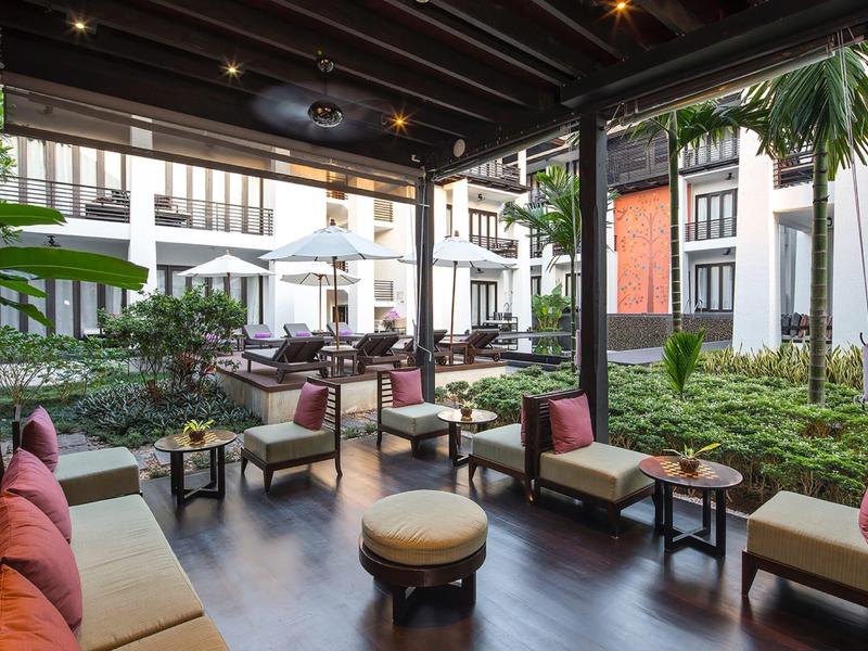 Gemütlicher Lounge-Bereich mit Sofas und Stühlen auf einer überdachten Terrasse neben einem Garten.