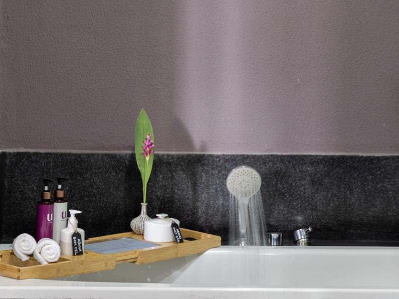 Badewanne mit Holzablage, Badesalz, Blume und Kosmetikflaschen in einem modernen Badezimmer.