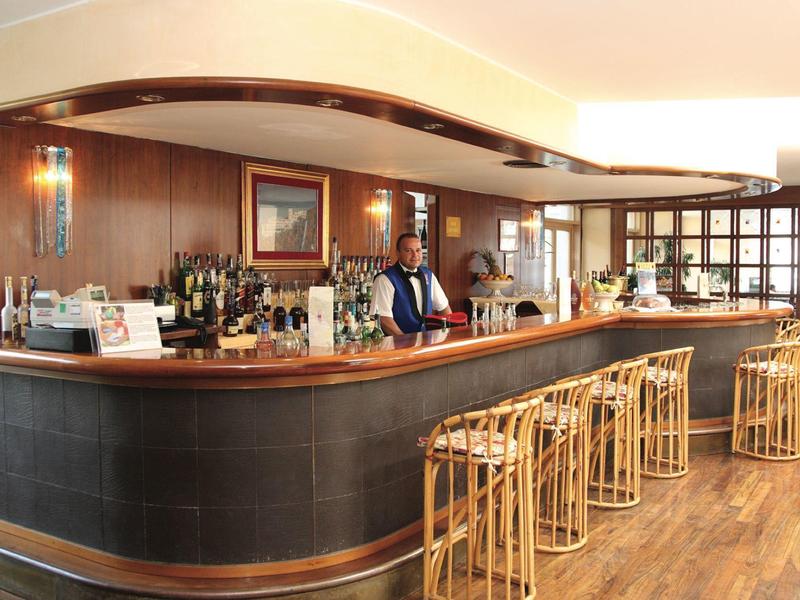 Bar mit Holzboden, Theke, Bambushockern und einem Barkeeper in heller, gemütlicher Atmosphäre.