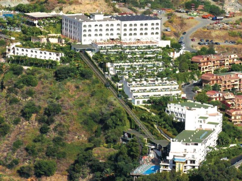 Mehrstöckige weiße Gebäude auf einem grünen Hügel mit umliegendem buschigen Gelände.