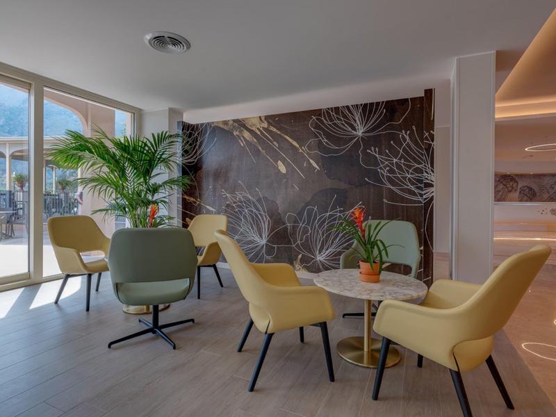 Helles Wohnzimmer mit gelben Sesseln, großem Fenster, Pflanze und dunkler Wand mit Blättermuster.