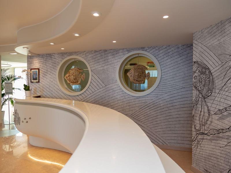 Schwungreiche weiße Theke vor grauer Wand mit runden Fenstern und Skateboard-Grafik.