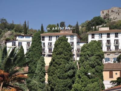 Mehrstöckiges Hotelgebäude mit Schriftzug "H. ARISTON" vor blauem Himmel und grünen Bäumen.