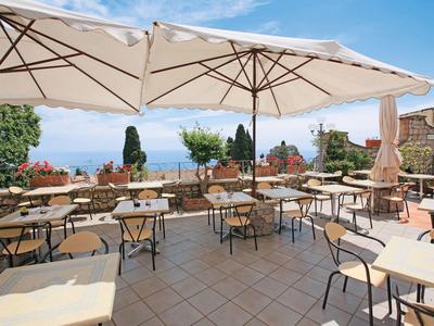Terrassenrestaurant mit Tischen, Stühlen, großen Sonnenschirmen und Meerblick im Hintergrund.