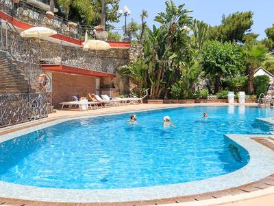 Großer blauer Pool mit Menschen, Liegestühlen und tropischer Bepflanzung im Hintergrund.