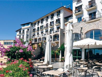 Außenbereich eines Hotels mit Tischen, Stühlen, Sonnenschirmen und blühenden Pflanzen bei klarem Himmel