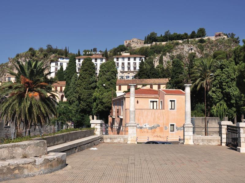 Blick auf historische Gebäude und Palmen an sonnigem Tag mit klar blauem Himmel.