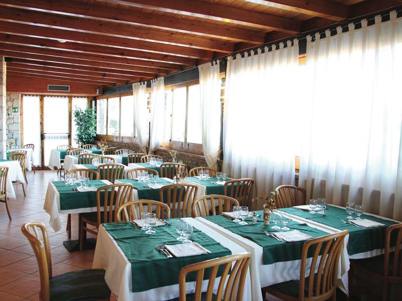 Heller Speisesaal mit grünen Tischdecken, Holzmöbeln und großen Fenstern mit weißen Vorhängen.