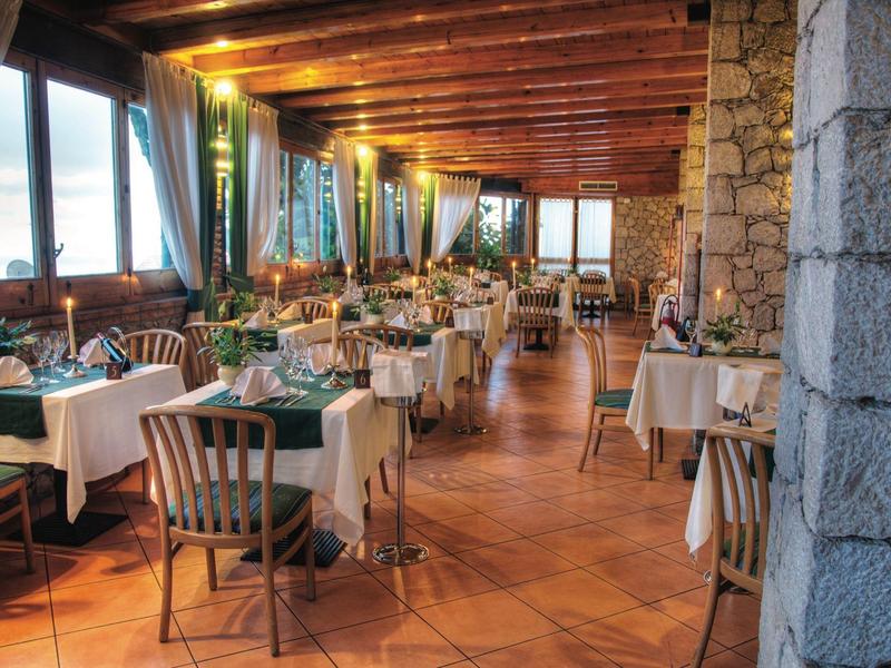 Gemütlicher Restaurantbereich mit Holzbalkendecke, weißen Tischdecken und Stühlen aus Holz.