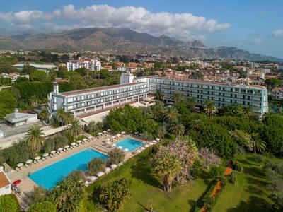 Großes Hotelgebäude mit Außenpool und umliegendem Garten in einer bergigen Landschaft.