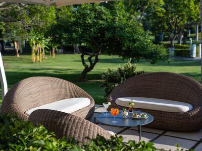 Drei dunkelbraune Korbsessel mit weißen Kissen auf einer Terrasse mit Blick auf einen grünen Garten.