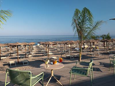 Blick auf einen Strand mit vielen Liegen, Sonnenschirmen und Sitzbereich am Meer.
