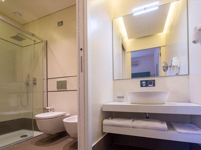 Modernes Badezimmer mit Dusche, WC, Bidet, Waschbecken und großem Spiegel in sanften Farben.