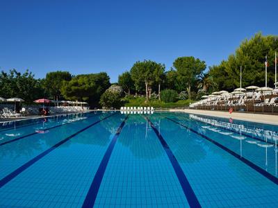 Klares beheiztes Schwimmbecken mit Bahnen, umgeben von Liegestühlen und Sonnenschirmen in hotelähnlicher Umgebung.
